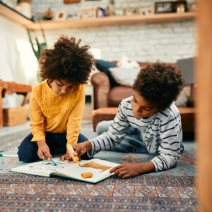 Creative black kids drawing while relaxing on the floor at home.