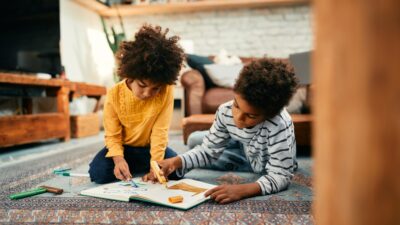 Creative black kids drawing while relaxing on the floor at home.