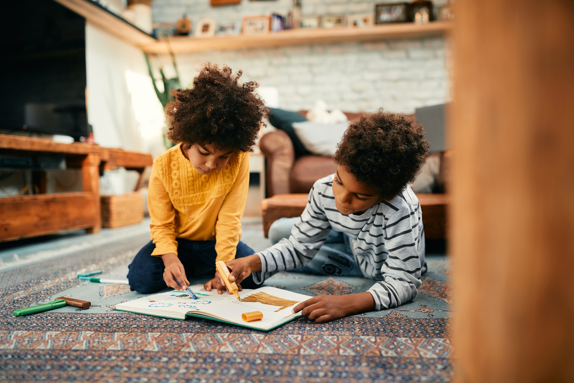 Creative black kids drawing while relaxing on the floor at home.