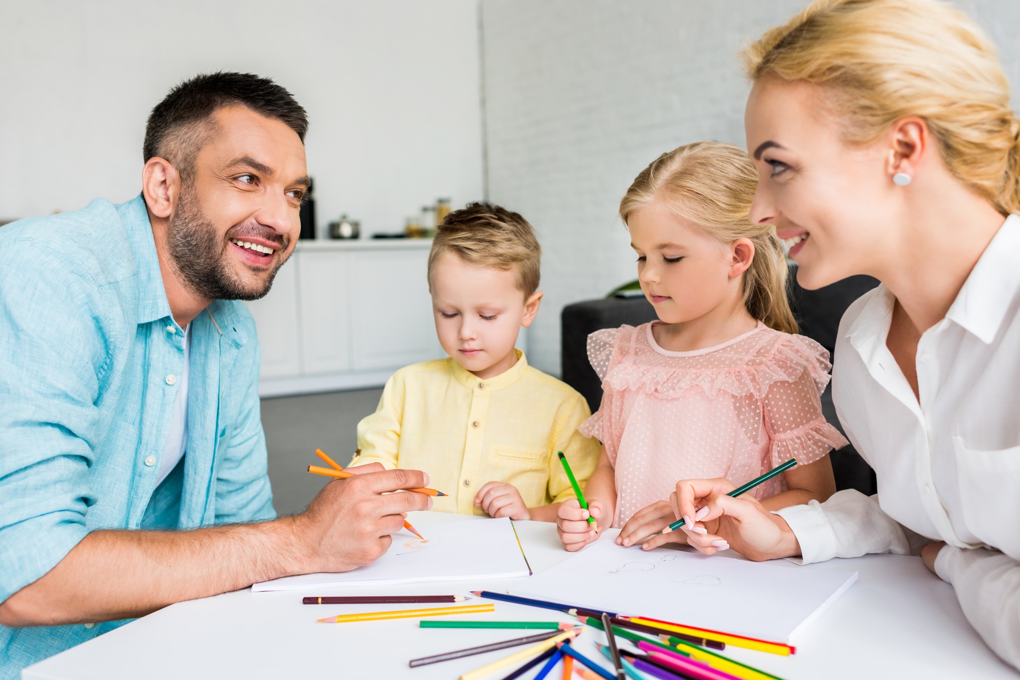 happy parents with two little kids drawing with colored pencils at home