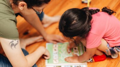 Mother and diverse daughter at home playing a game from a book, bonding, early education