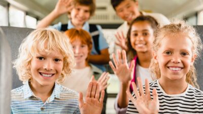 Happy mixed-race multiethnic schoolchildren classmates kids pupils sitting inside school bus